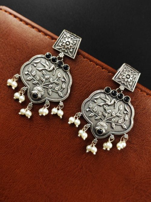 A close-up view of silver floral art earrings dangling elegantly.