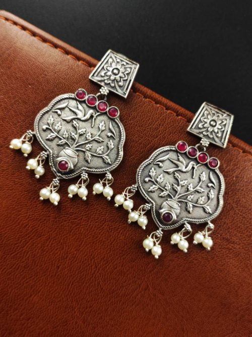 A close-up view of silver floral art earrings dangling elegantly.