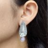 Traditional oxidized silver stud earrings with floral art, pearl, and stone work.