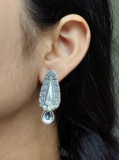 Traditional oxidized silver stud earrings with floral art, pearl, and stone work.